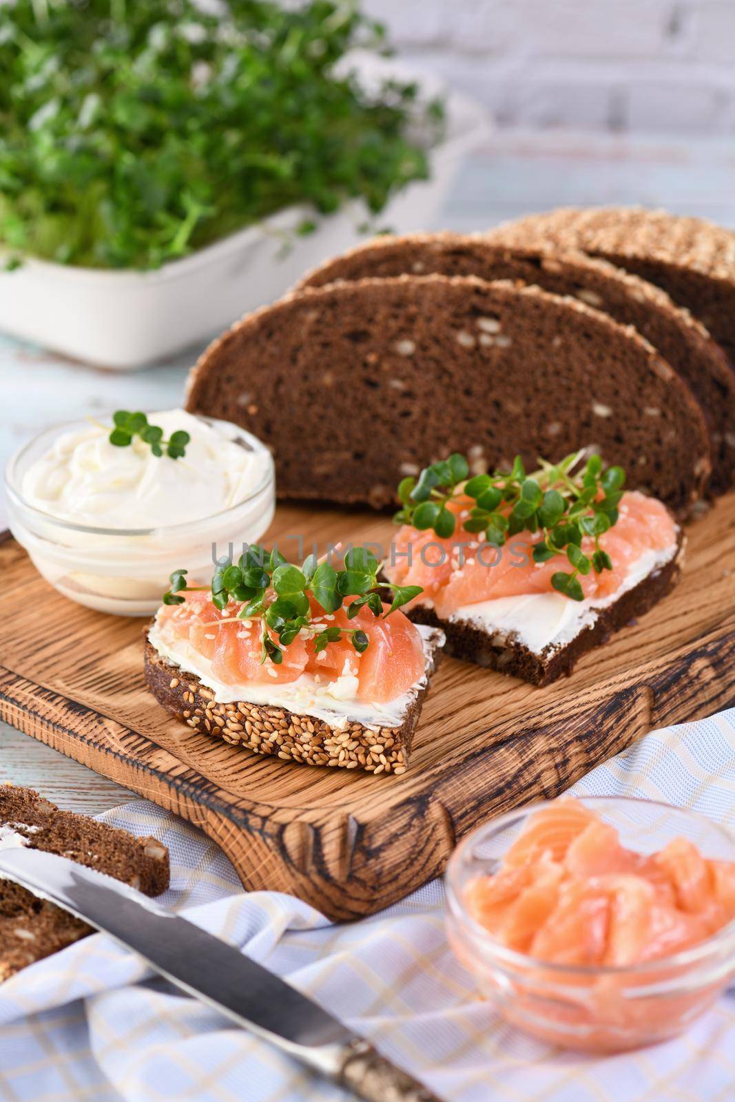 Open sandwich with cheese cream on a slice of rye bread with cereals, slices of marinated salmon, and radish sprouts.