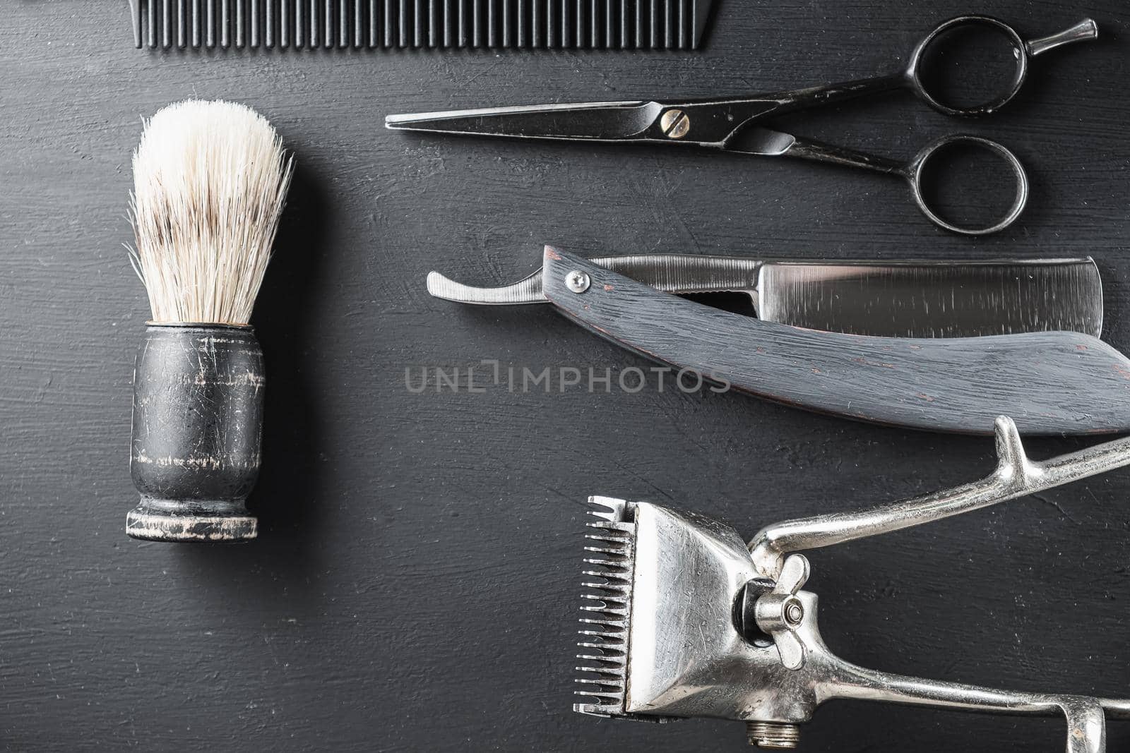 On a black dusty surface are old barber tools. Vintage manual hair clipper comb razor shaving brush shaving brush hairdressing scissors. black monochrome. horizontal. top view. flat lay.