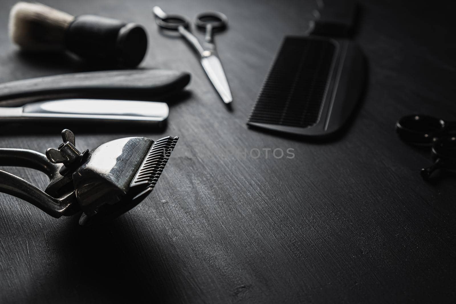 On a black dusty surface are old barber tools. Vintage manual hair clipper comb razor shaving brush shaving brush hairdressing scissors. black monochrome. horizontal.