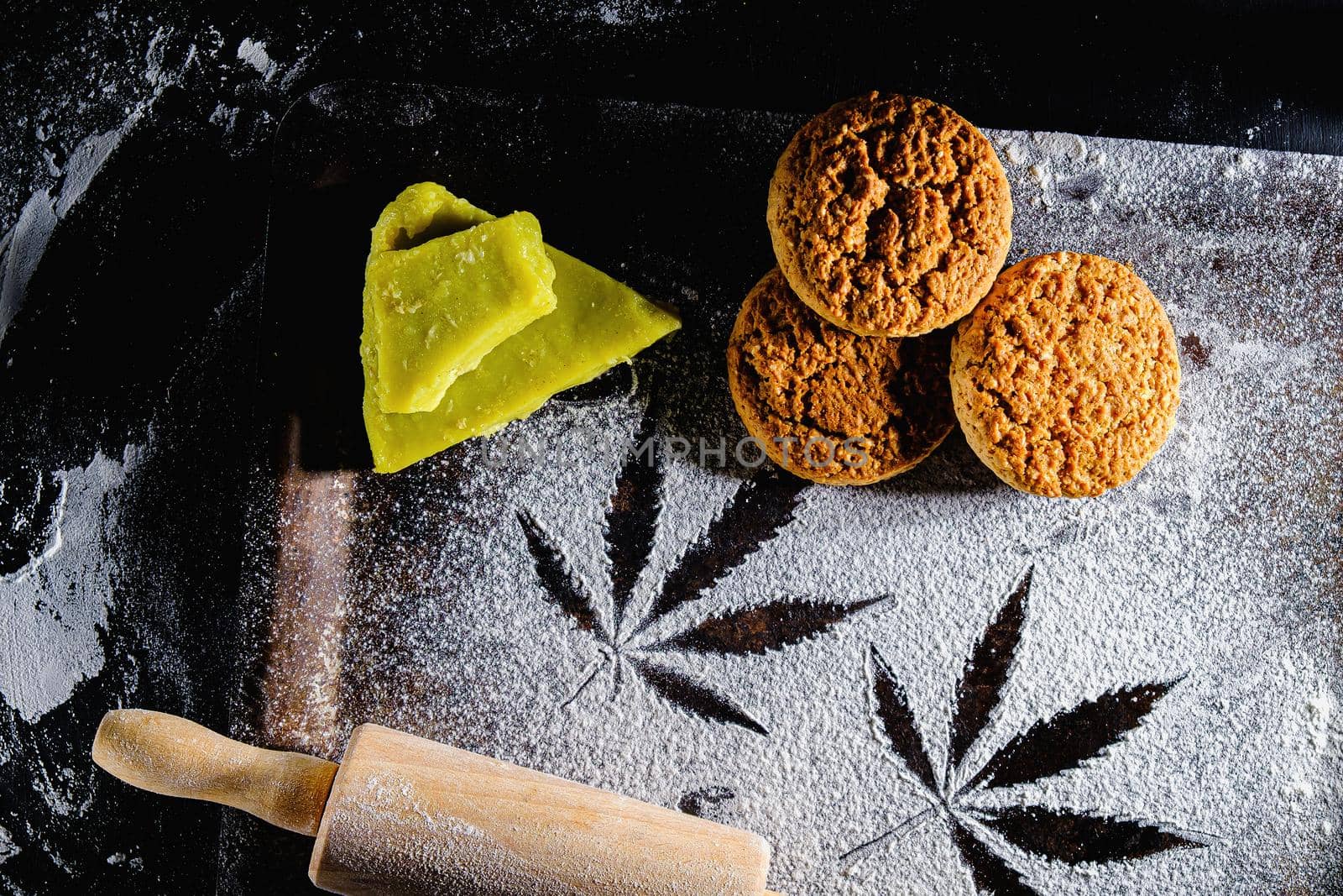 traces of marijuana leaves on flour, and rolling pin and three cookies and cannabis butter. on a rusty pan. top view flat lay. Horizontal orientation