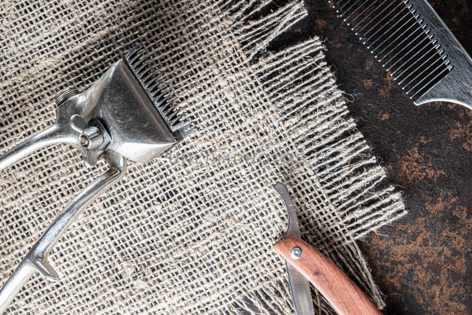 vintage barber tools dangerous razor, hairdressing scissors, old manual clipper, metal comb, shaving brush. Lies on a rough burlap sack background. Horizontal. top view, flat lay. copy space