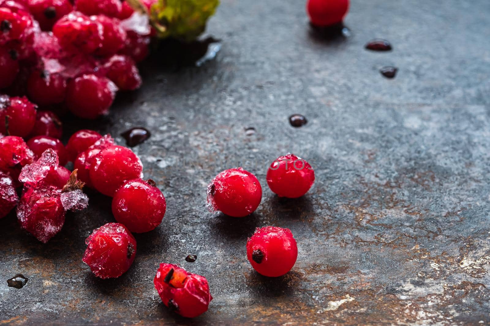 scattered frozen ice red currants closeup lie on a rusty surface. copy space. horizontal orientation.