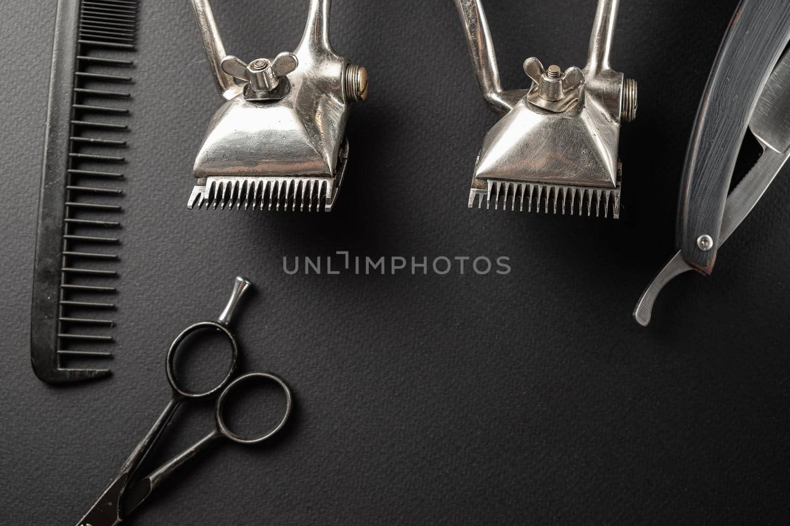 On a black surface are old hairdresser tools. Two vintage hand-held hair clippers, combs, razor, hairdressing scissors, shaving brush. black monochrome. horizontal orientation. top view, flat lay
