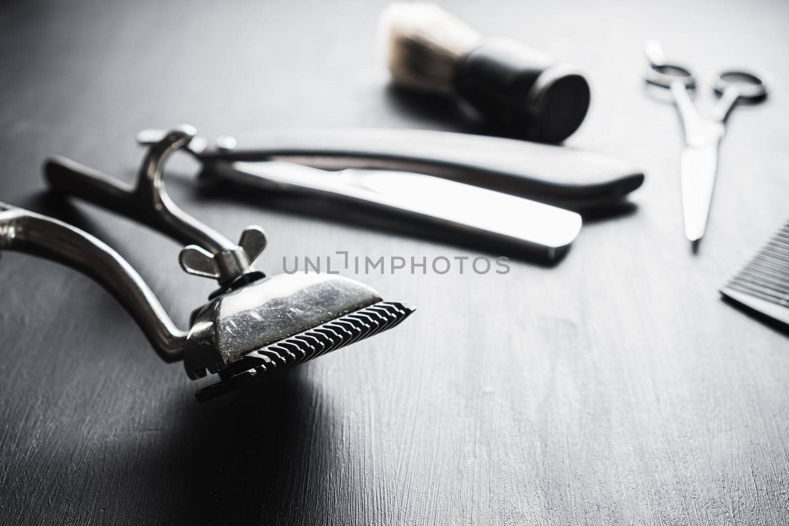 On a black dusty surface are old barber tools. Vintage manual hair clipper comb razor shaving brush shaving brush hairdressing scissors. black monochrome. horizontal.