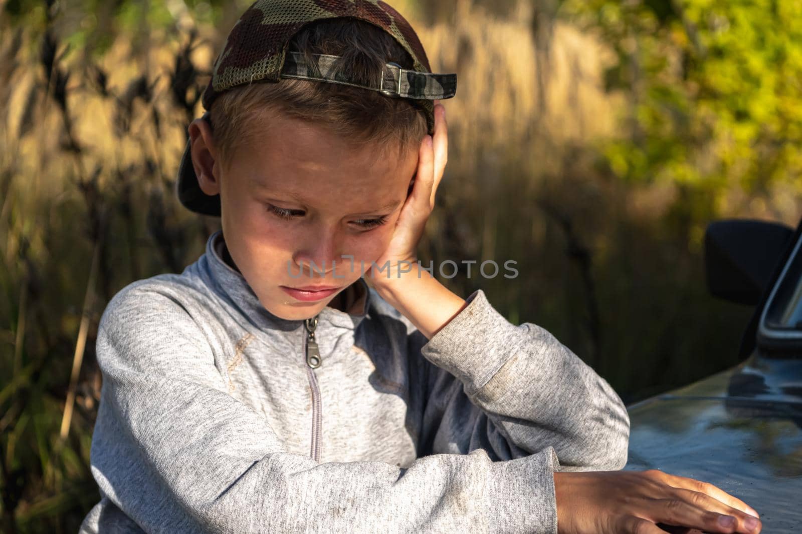 a cute six year old boy stands by the car against the background of autumn grass.. horizontal orientation.