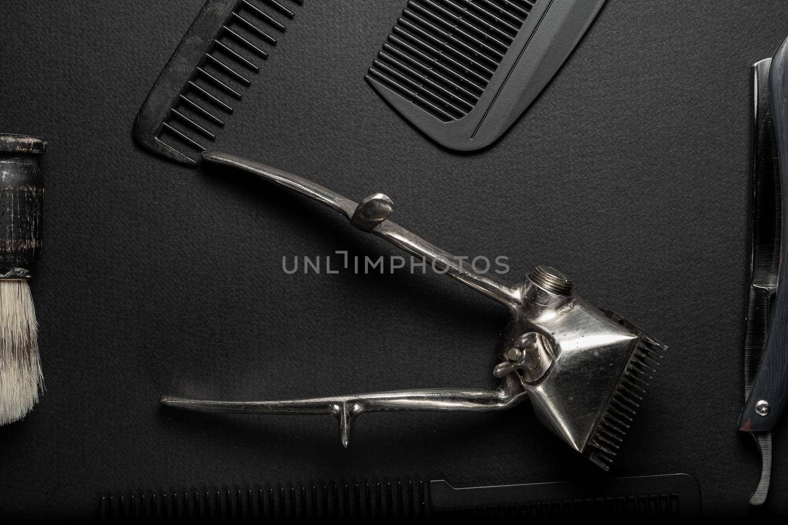 On a black surface are old hairdresser tools. vintage hand-held hair clipper, hairdressing scissors, combs, razor, shaving brush. black monochrome. horizontal orientation. top view flat ley