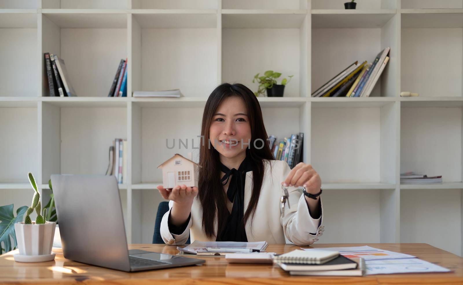 Portrait asian businesswoman real estate hand holding house model and key, house sell broker concept. by nateemee