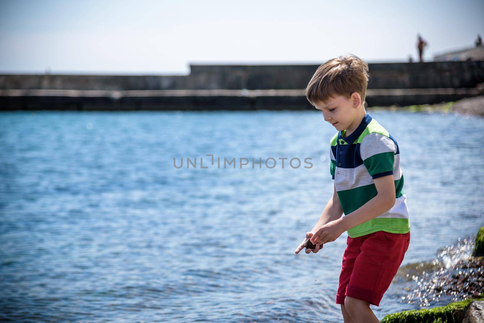 The little boy by the sea throws stones in water. Relaxation and vacation with kids. Happy childhood by Kobysh