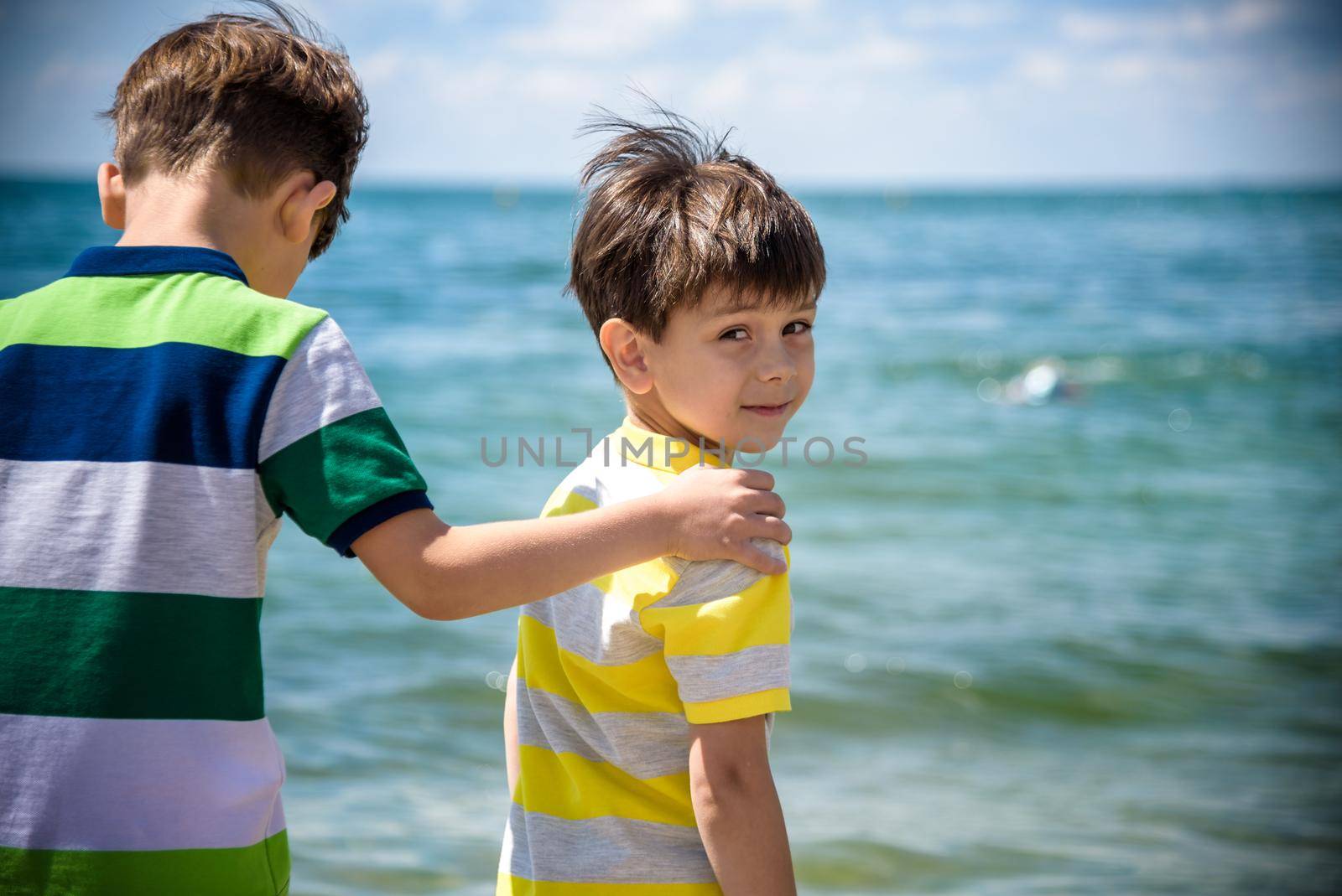 Two adorable little kid boys standing on lonely ocean beach. Child playing and looking on horizon. View from back. Preschool children sibling brother best friends enjoying summer vacations on sea.