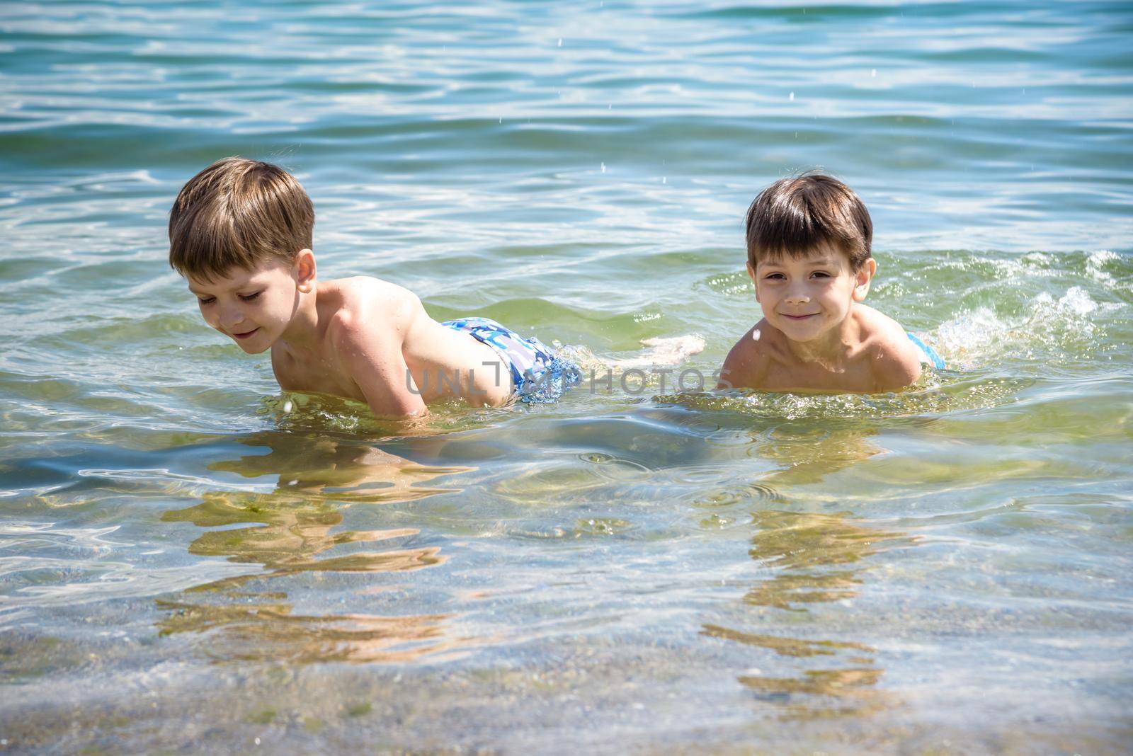 Happy family playing in blue water of swimming pool on a tropical resort at the sea. Summer vacations concept. Two brother kids are best friends.