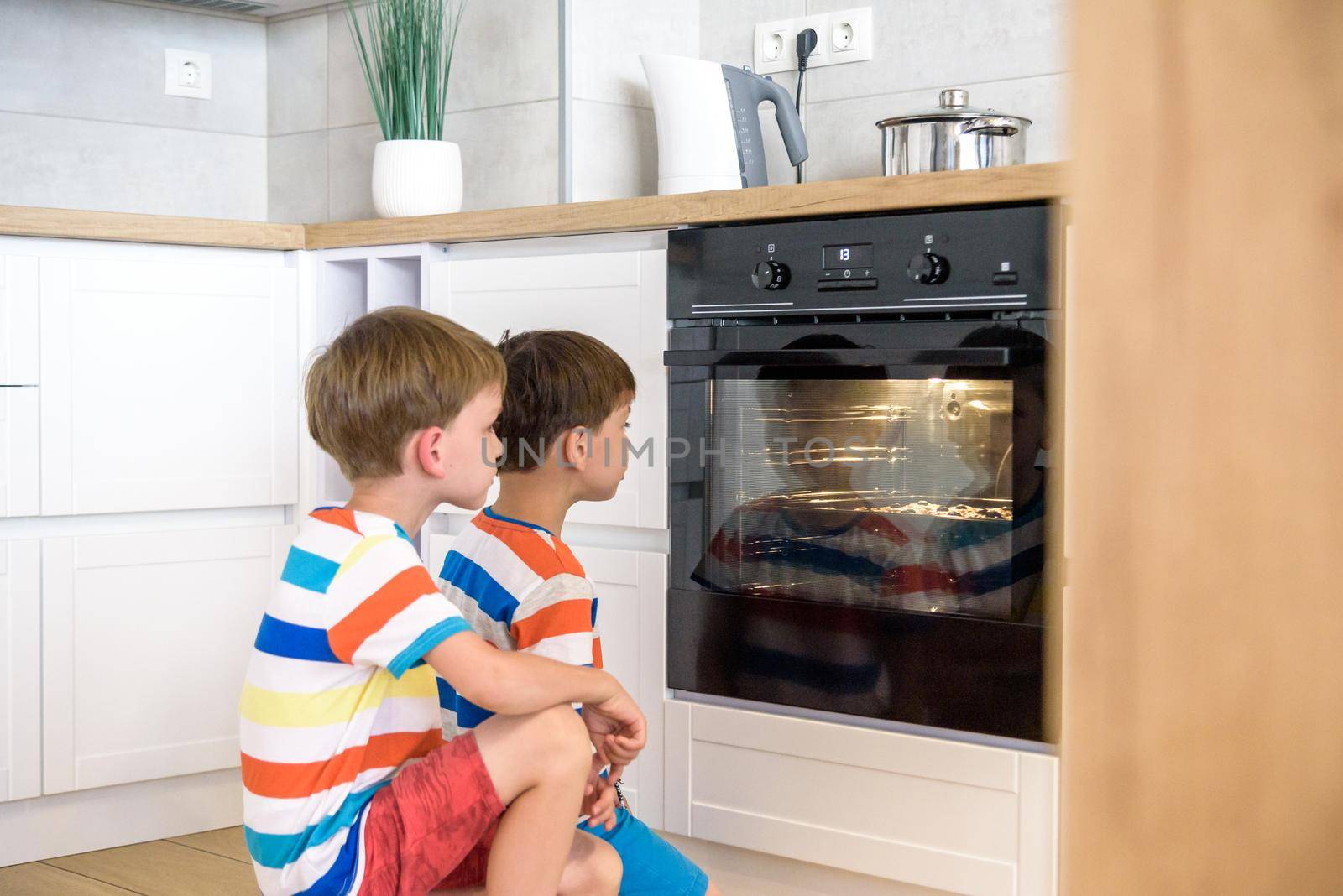 Kids playing in kitchen and waiting for preparation of biscuits in oven. two brothers sibling boys cooking at home.