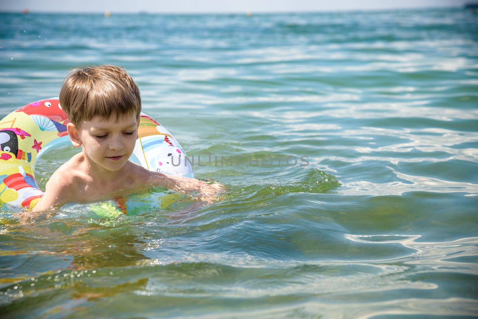 Happy little boy playing with colorful inflatable ring in outdoor swimming sear river lake or pool on hot summer day. Kids learn to swim and having fun.