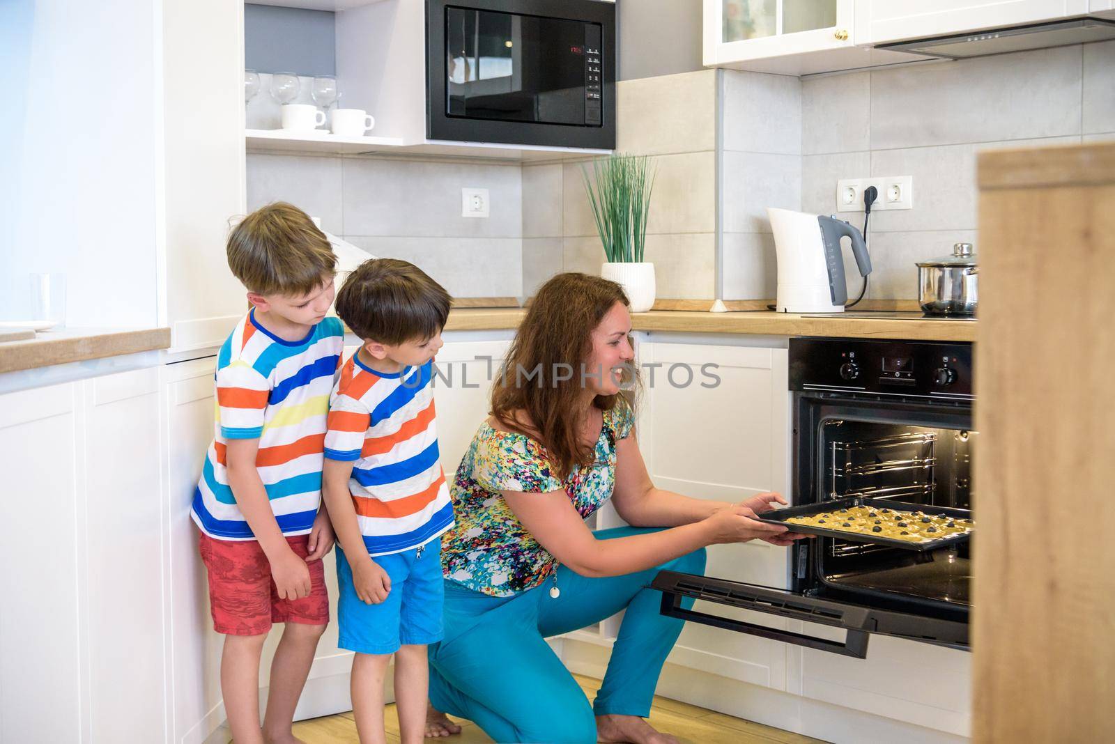 Kids and mother baking. Two children and parent cooking. Little boy and brother boy cook and bake in a white kitchen with modern oven. Sibling Brother making a cookies for dinner.