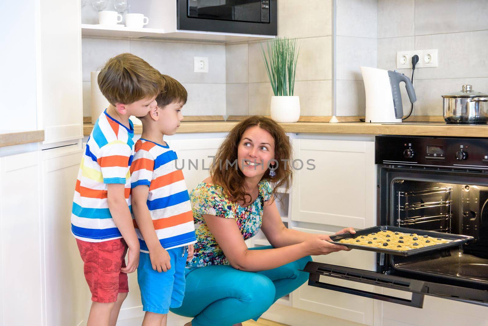 Kids and mother baking. Two children and parent cooking. Little boy and brother boy cook and bake in a white kitchen with modern oven. Sibling Brother making a cookies for dinner.