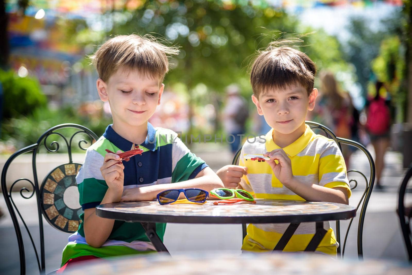 Two little kid boys waiting on table for healthy breakfast in hotel restaurant or city cafe. Child sit on comfortable chair play with toy aircraft, relaxed, enjoy their vacation. Summer holiday with children concept.