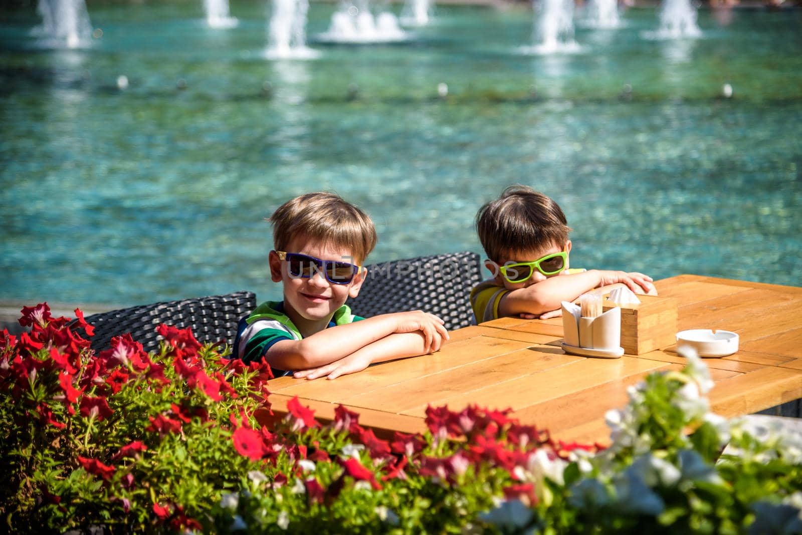 Two little kid boys waiting on table for healthy breakfast in hotel restaurant or city cafe. Summer holiday with children concept.