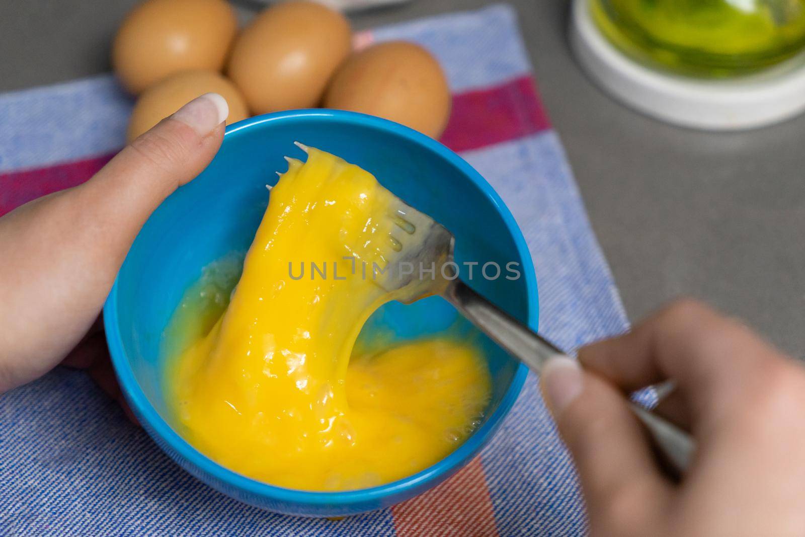 beating hen's eggs in a blue bowl with a fork by CatPhotography