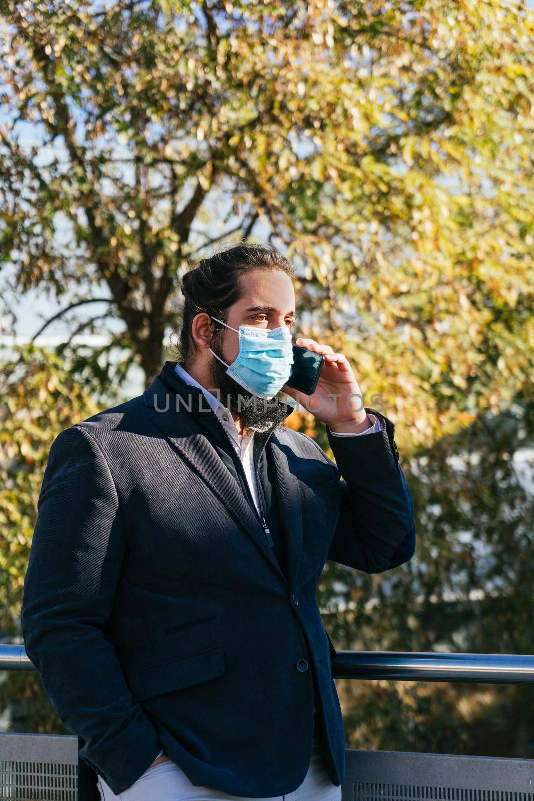 Young business man talking mobile with face mask by CatPhotography