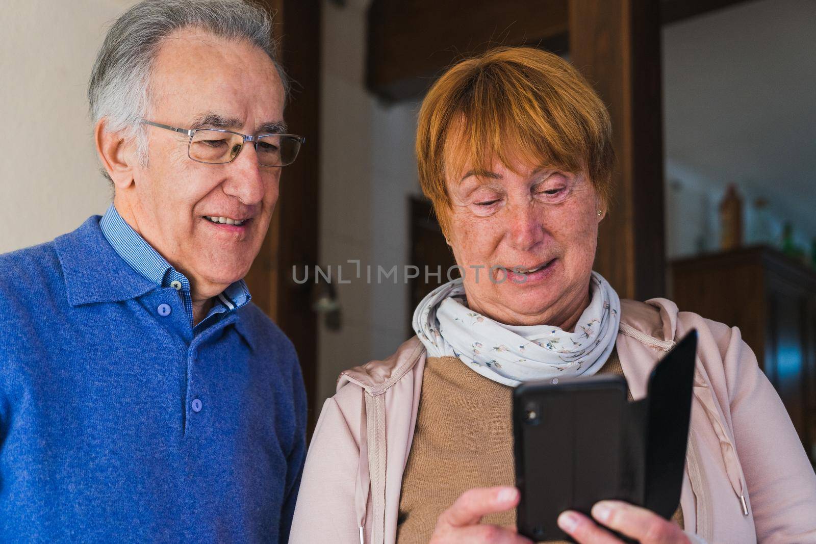 Old couple looking at mobile in house by CatPhotography