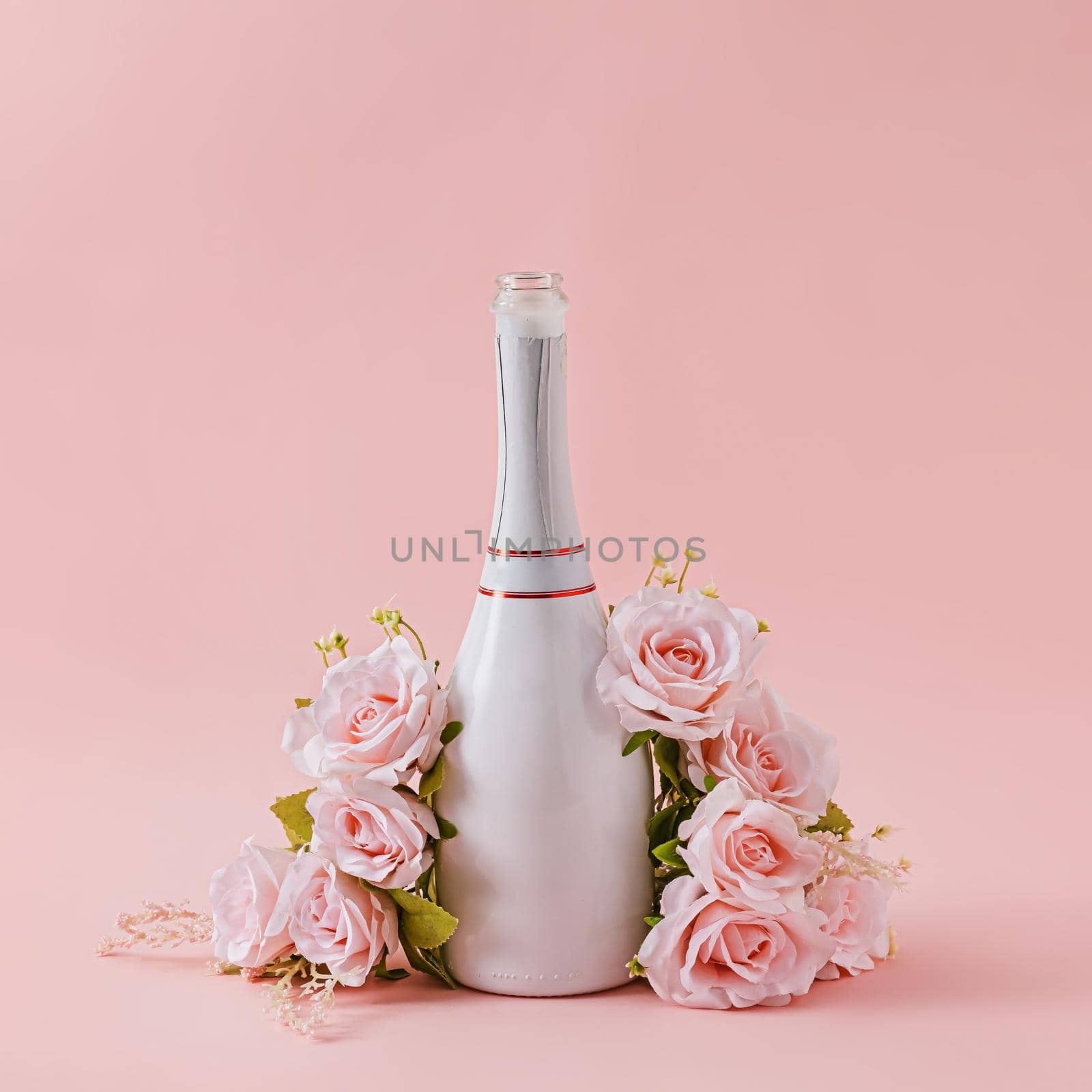 White bottle of champagne with roses over a pink background by sergii_gnatiuk