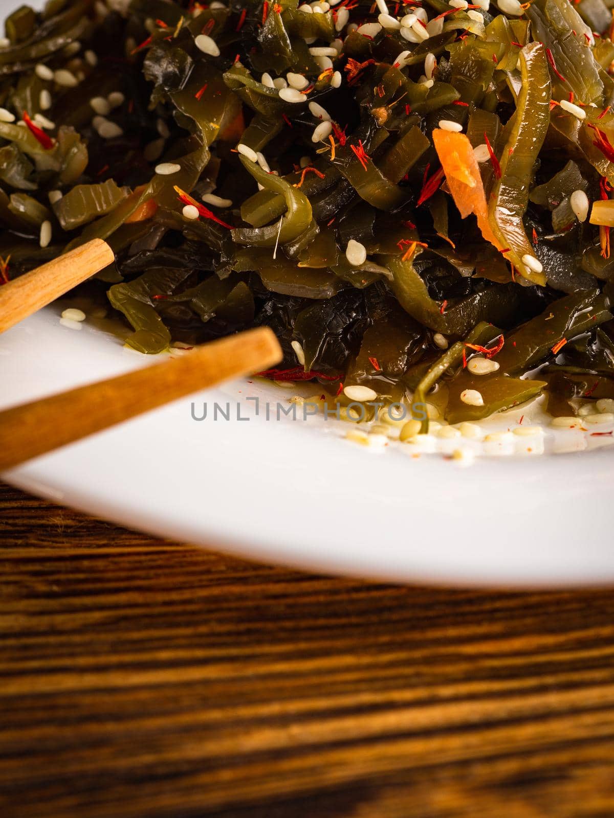 Seaweed salad with sesame seeds is on a white plate. Wooden background. vertical.