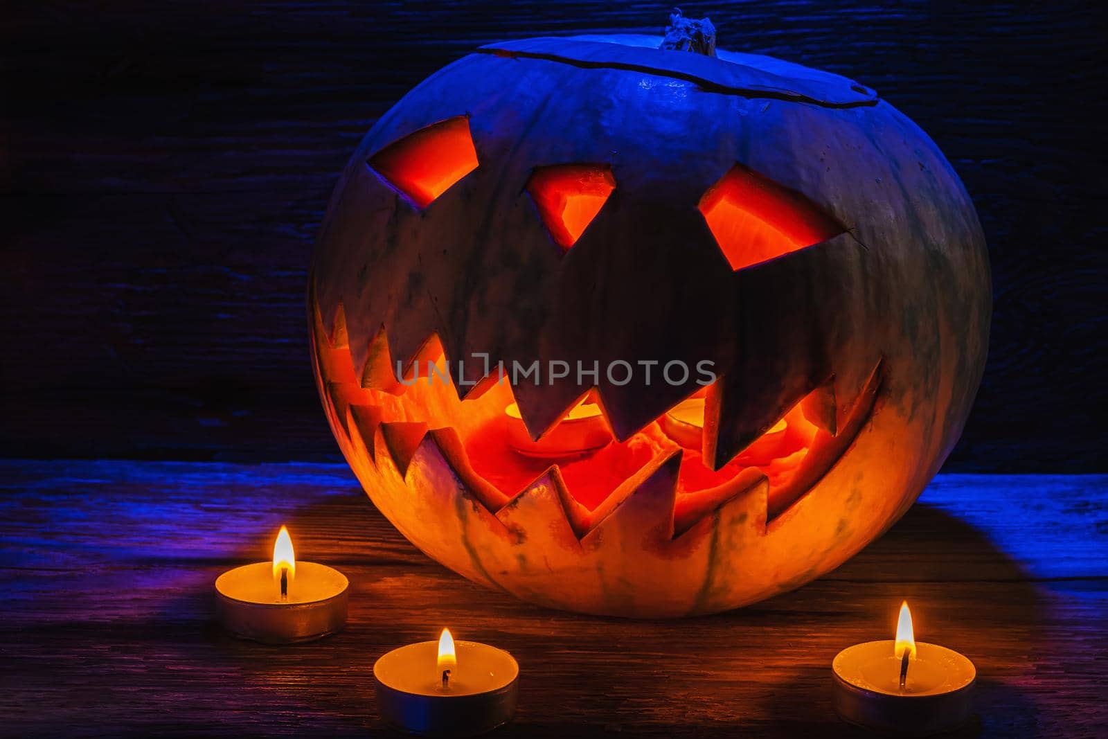 Jack O' Lantern Glowing In Fantasy Night. Halloween. candles are burning nearby. On old wooden background. dramatic frame. horizontal orientation
