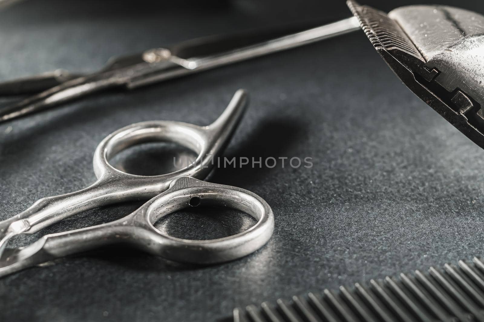 On a black surface are old barber tools. Vintage manual hair clipper, comb, razor, hairdressing scissors. black monochrome. Close-up. Barbershop background. contrast shadows. horizontal orientation