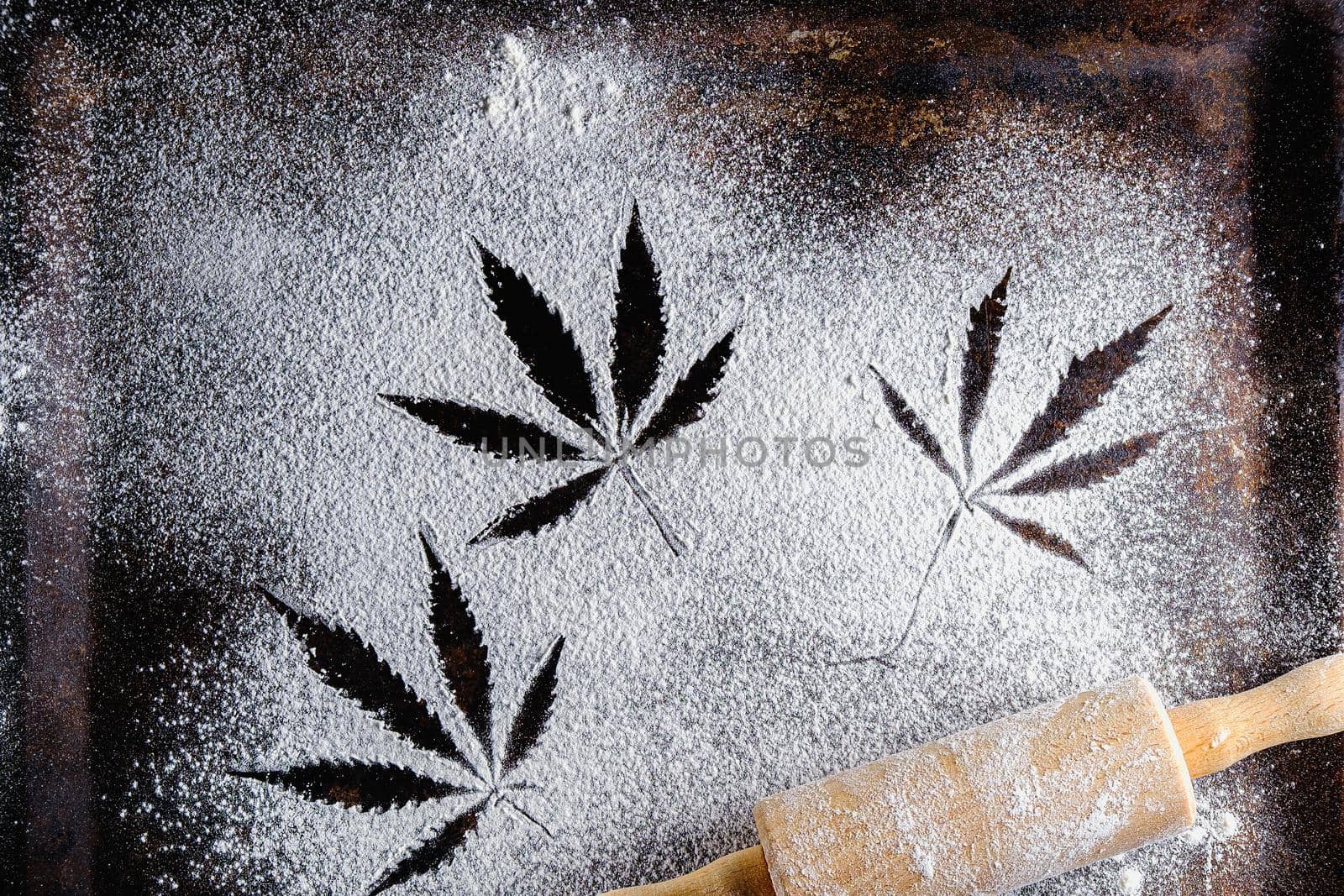 traces of marijuana leaves on flour, and rolling pin and three cookies and cannabis butter. on a rusty pan. top view flat lay. Horizontal orientation