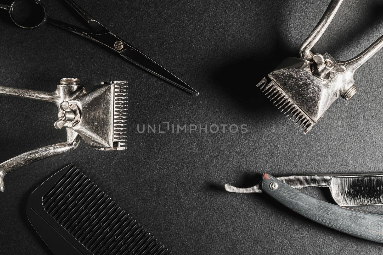 On a black surface are old barber tools. two vintage manual hair clipper, comb, razor, hairdressing scissors. black monochrome. Close-up. Barbershop background. horizontal orientation. Top view, flat lay.