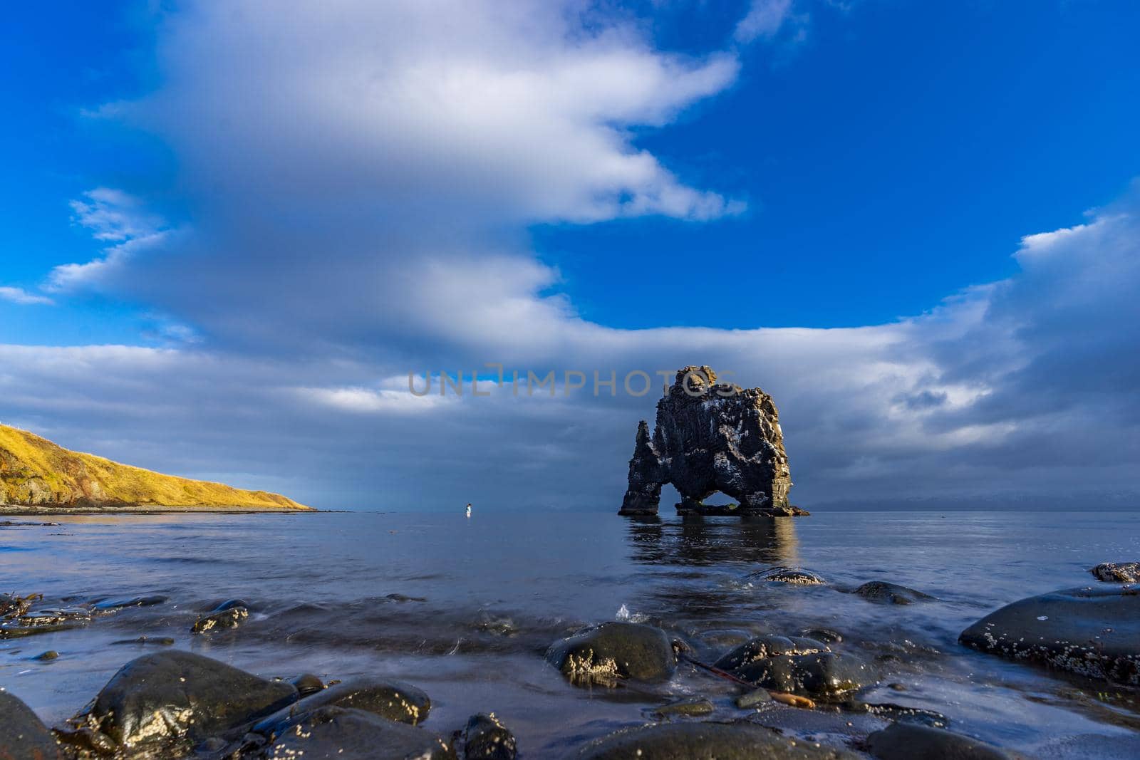 Blurred tourist approaching to Hvitserkur dragon drinking boulder, long exposure in Iceland