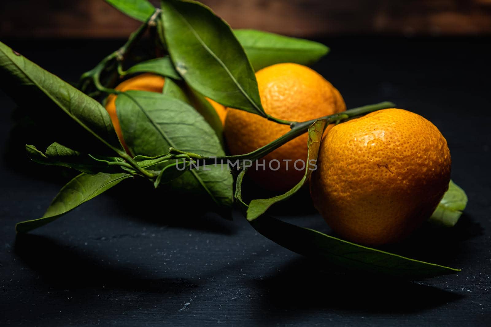 on a dark surface are three tangerines with leaves. Horizontal orientation.