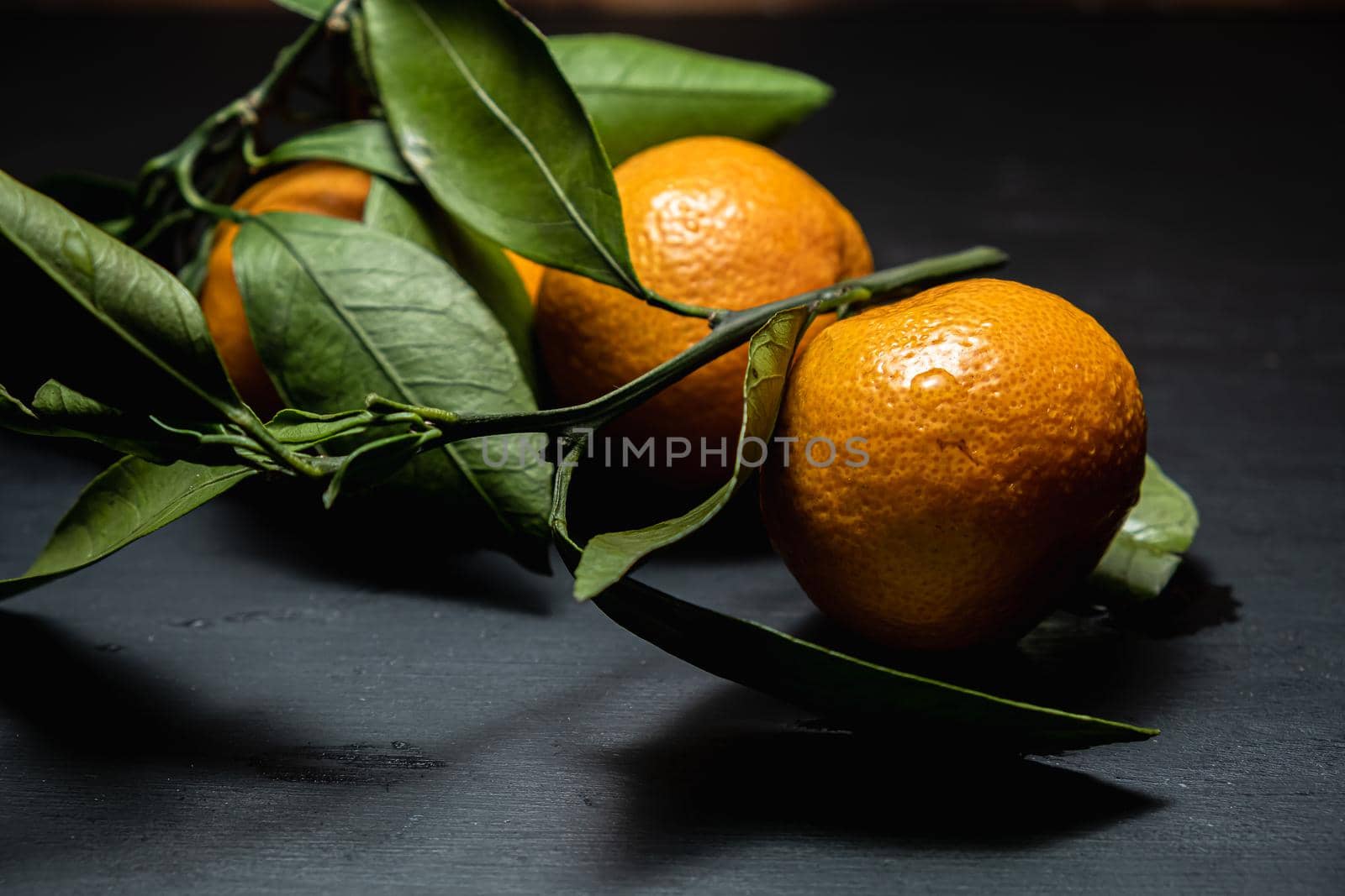 on a dark surface are three tangerines with leaves. Horizontal orientation.