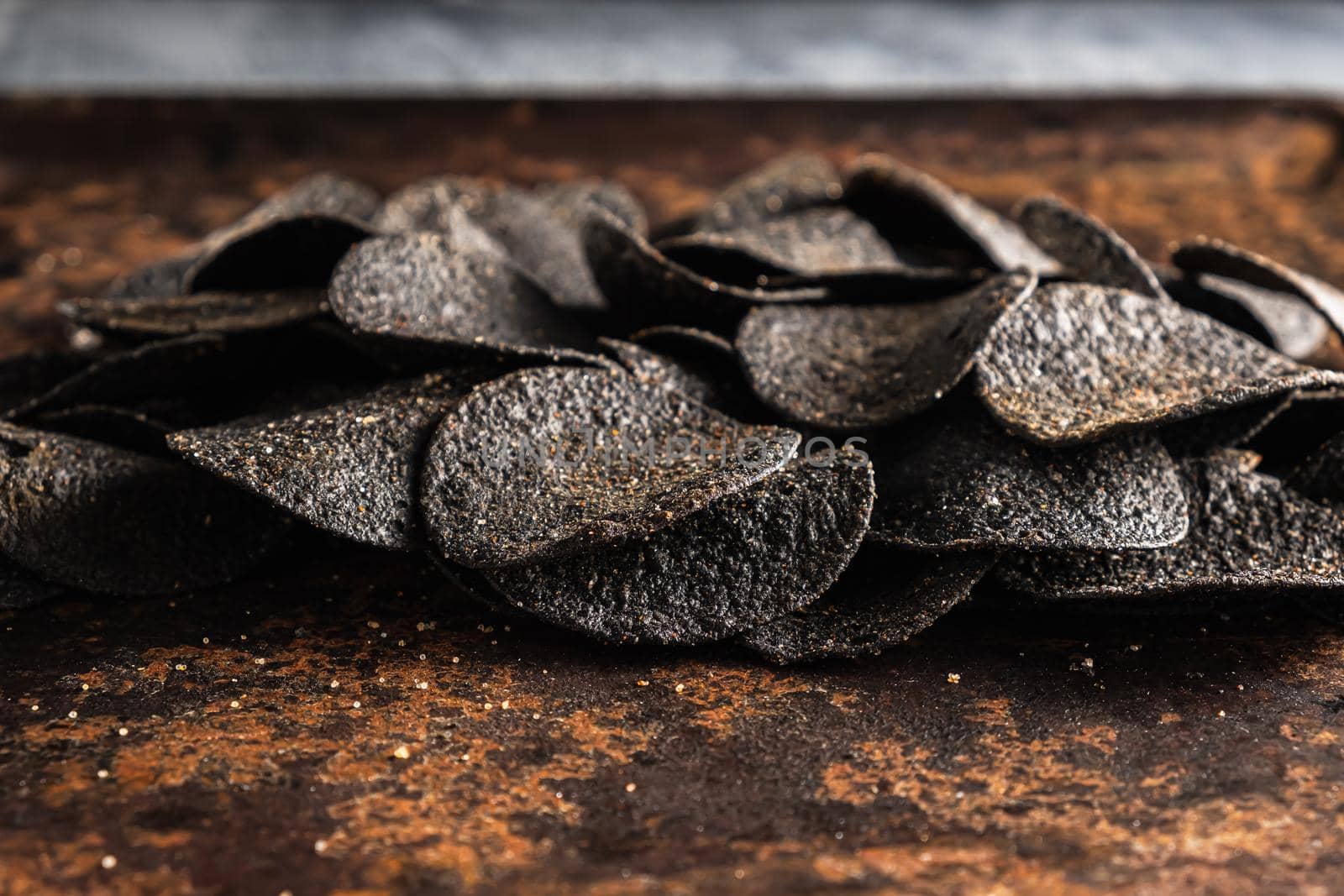 a lot of black chips with spices on an old rusty baking sheet