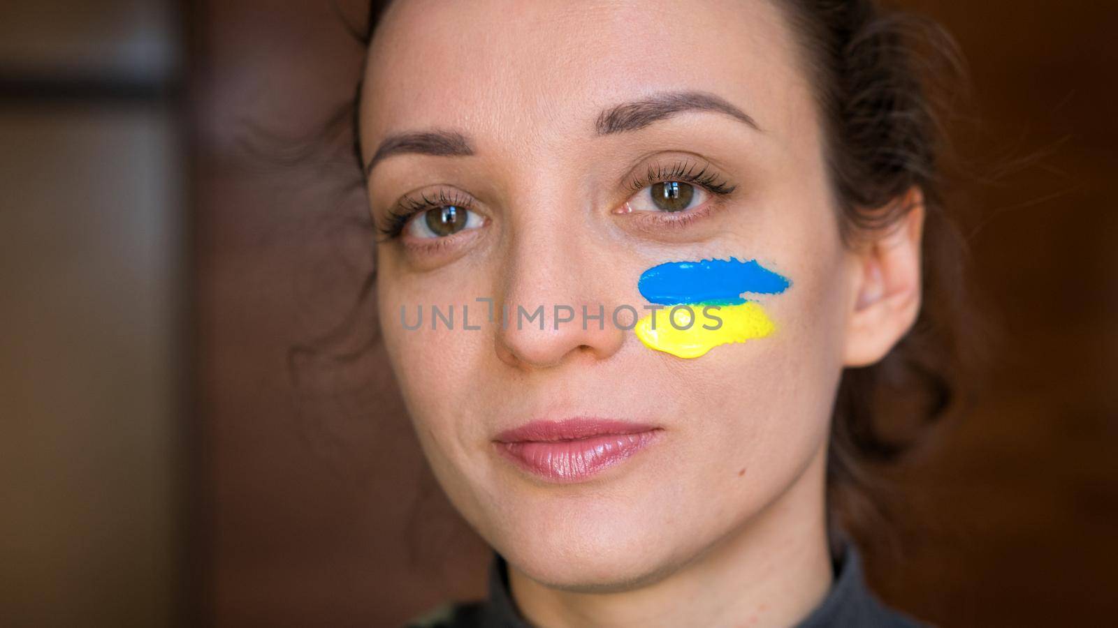 Indoor portrait of young girl with blue and yellow ukrainian flag on her cheek wearing military uniform, mandatory conscription in Ukraine, equality concepts.