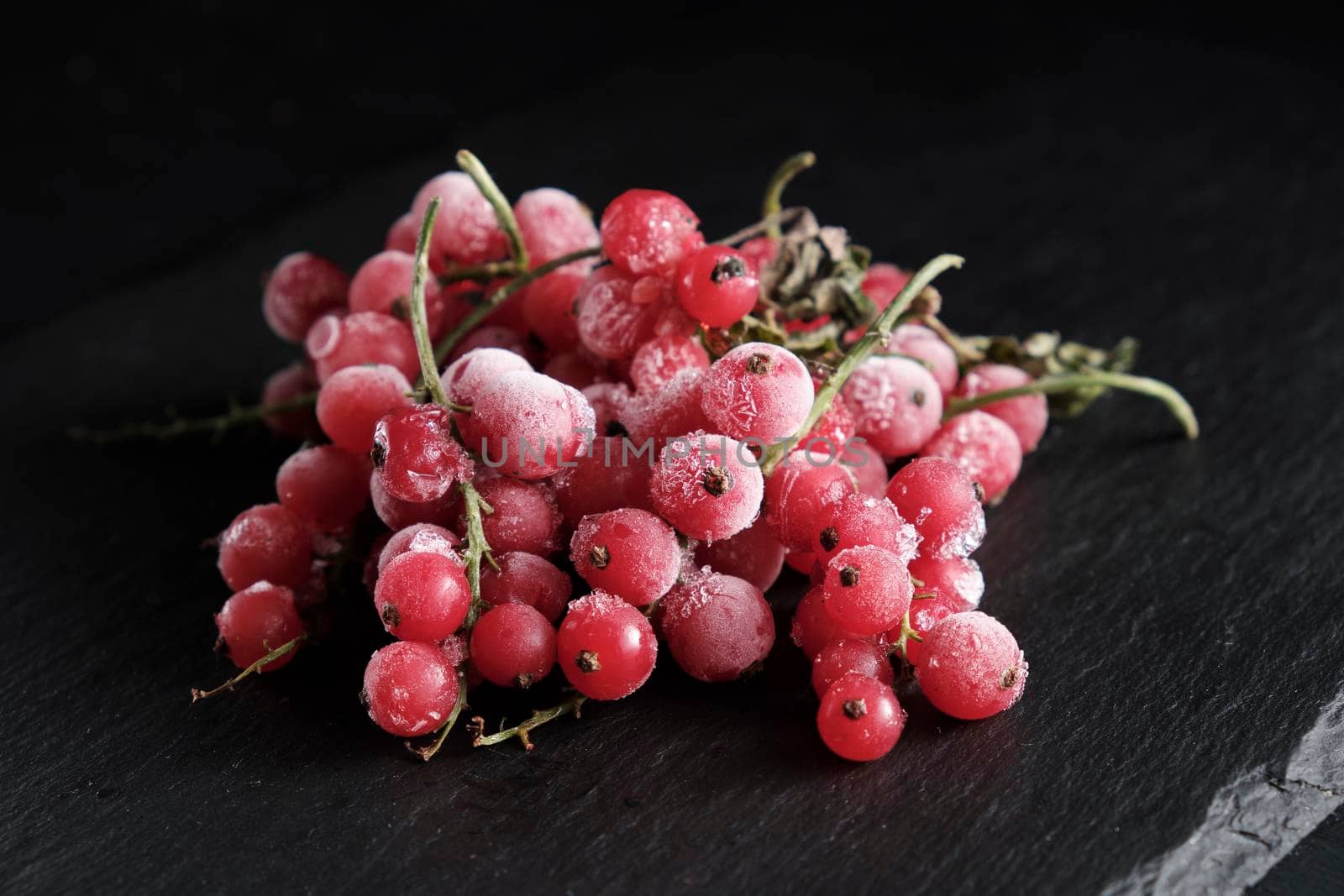 organic natural frozen berries red currants covered with hoarfrost scattered on a slate dish. Horizontal orientation. Close-up.