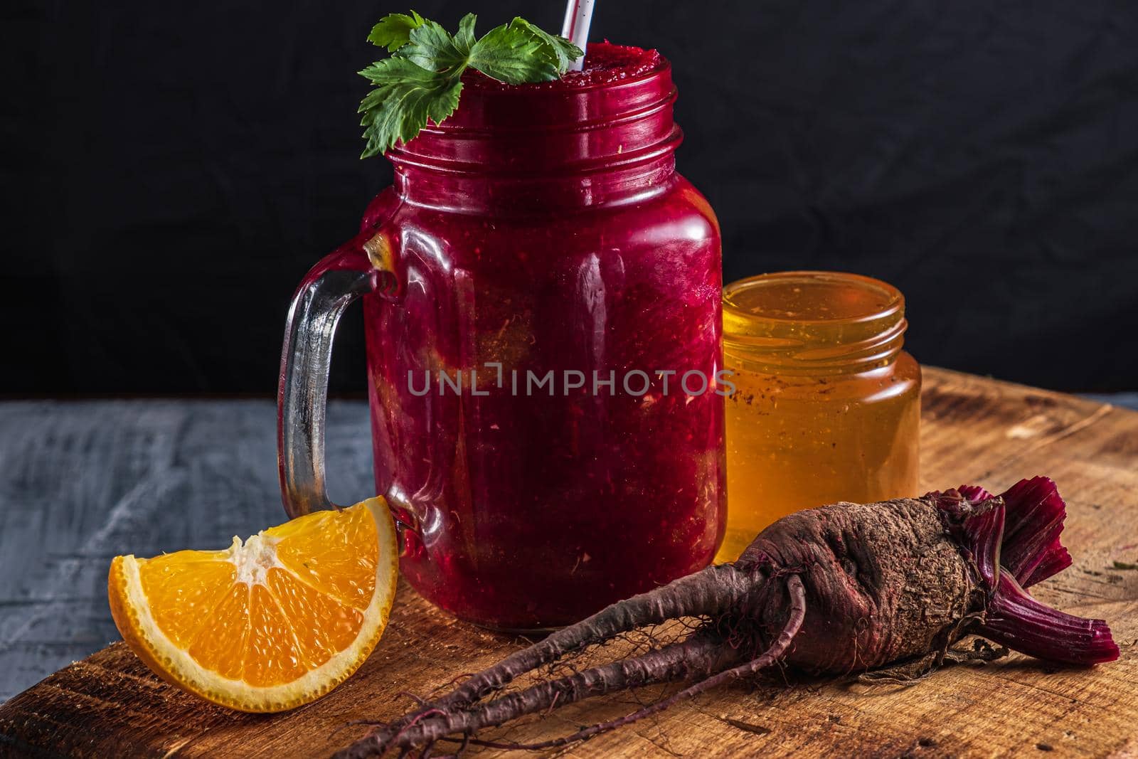 Smoothie consists of beets, orange, celery in a mason jar. There is a jar of honey next to it, a beet root, a piece of pumpkin and pieces of orange. on a thick wooden board. horizontal orientation.