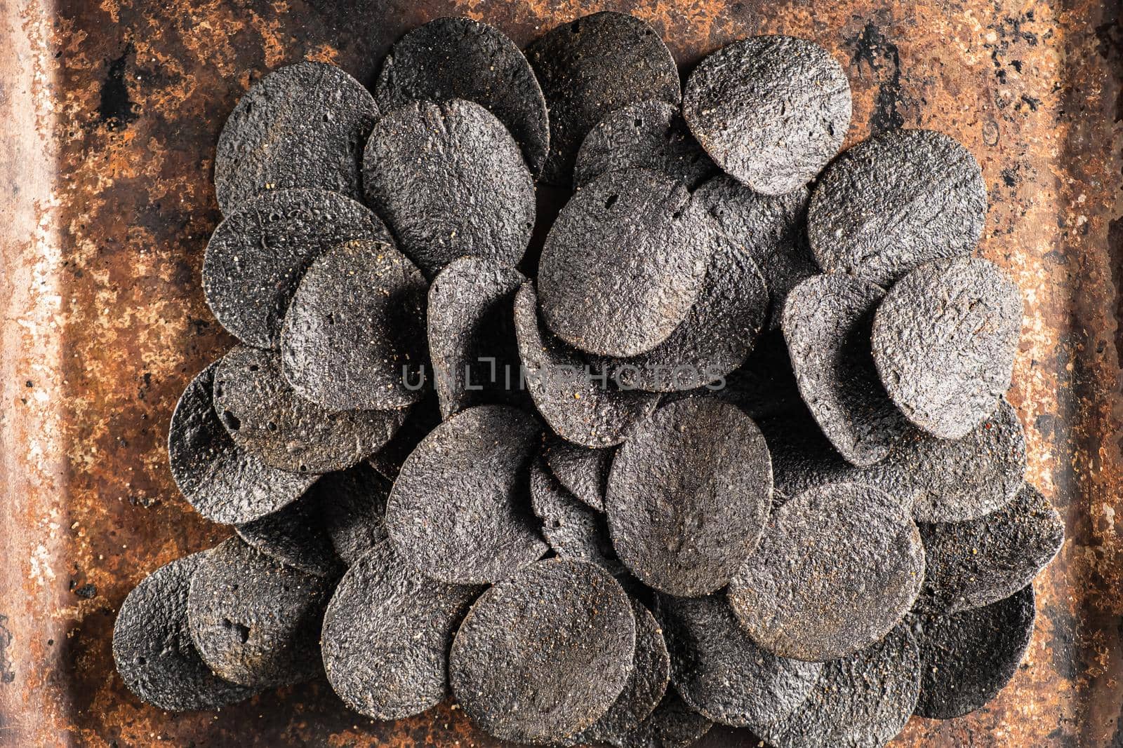 a lot of black chips with spices on an old rusty baking sheet