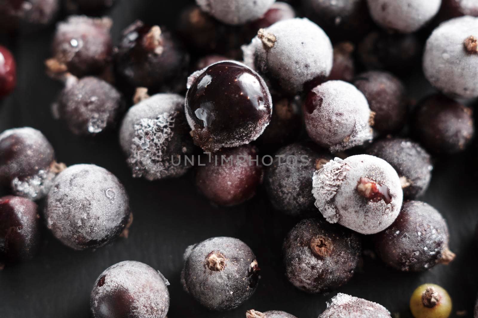 Organic natural frozen blackcurrant berries covered with hoarfrost scattered on a slate dish. Horizontal orientation. Close-up.