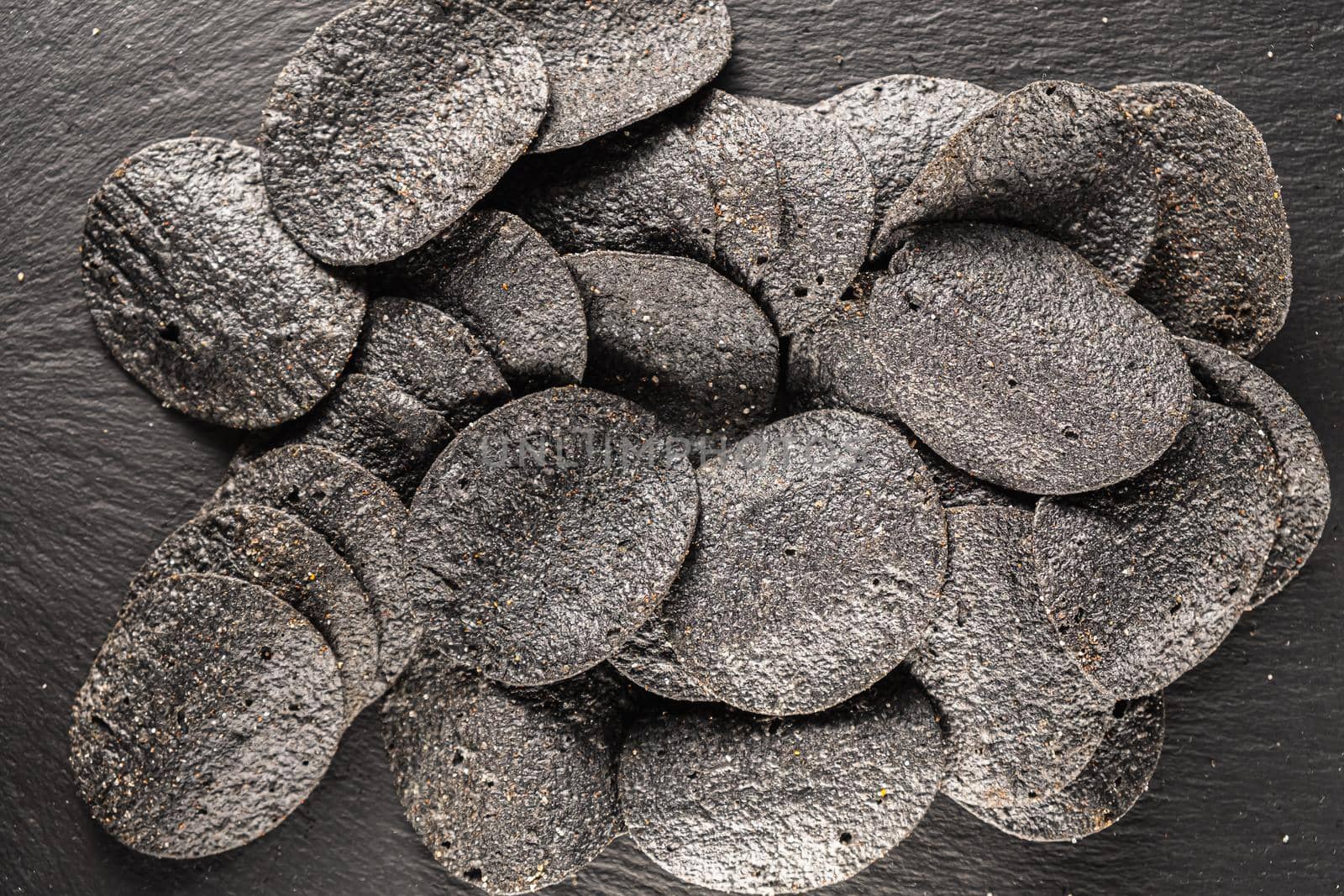 background of many black chips with spices on a slate dish. close-up.