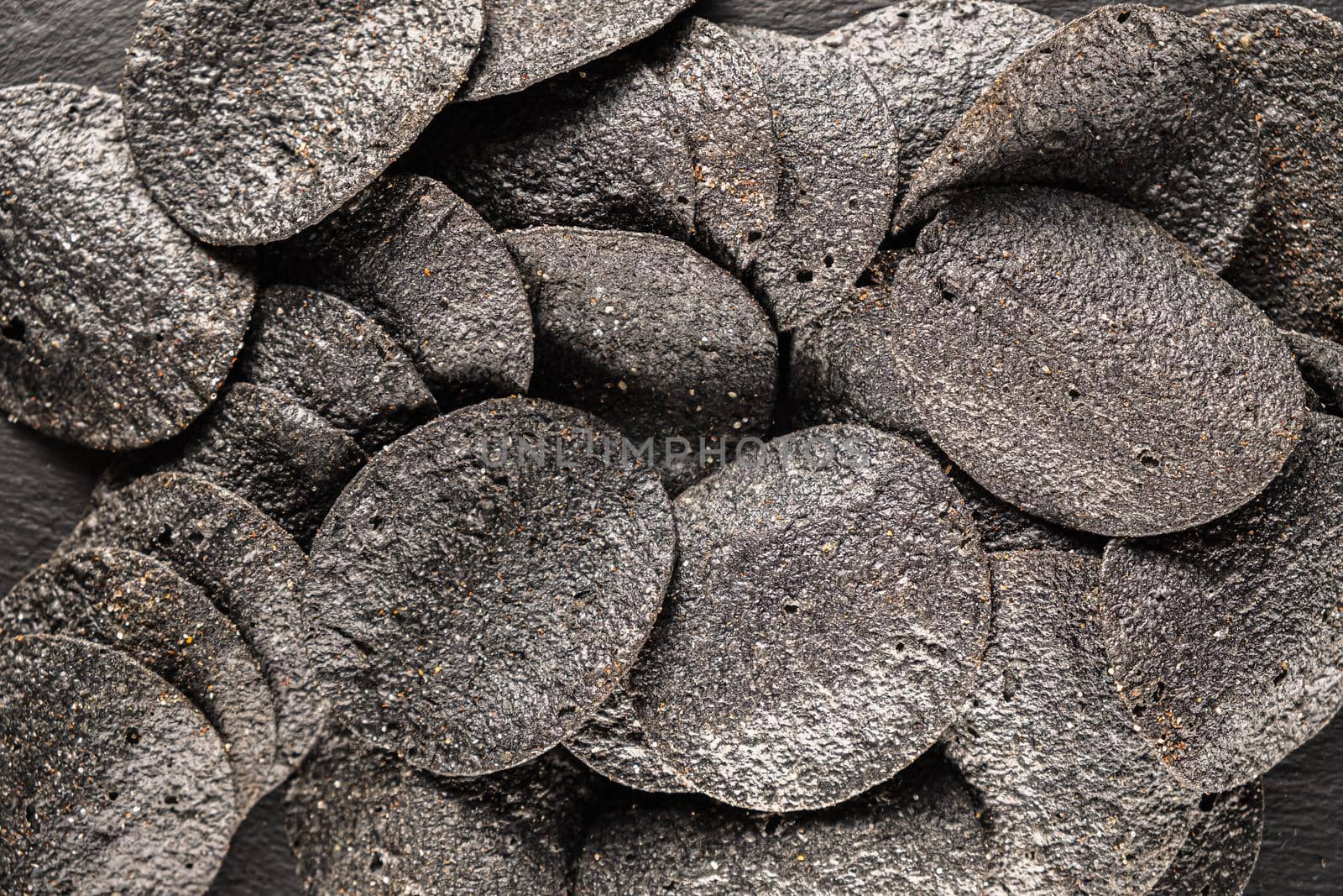 background of many black chips with spices on a slate dish. close-up.