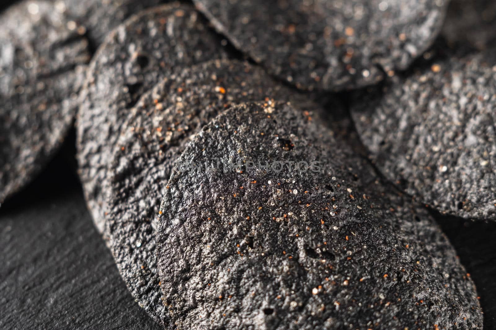 background of many black chips with spices on a slate dish. close-up.