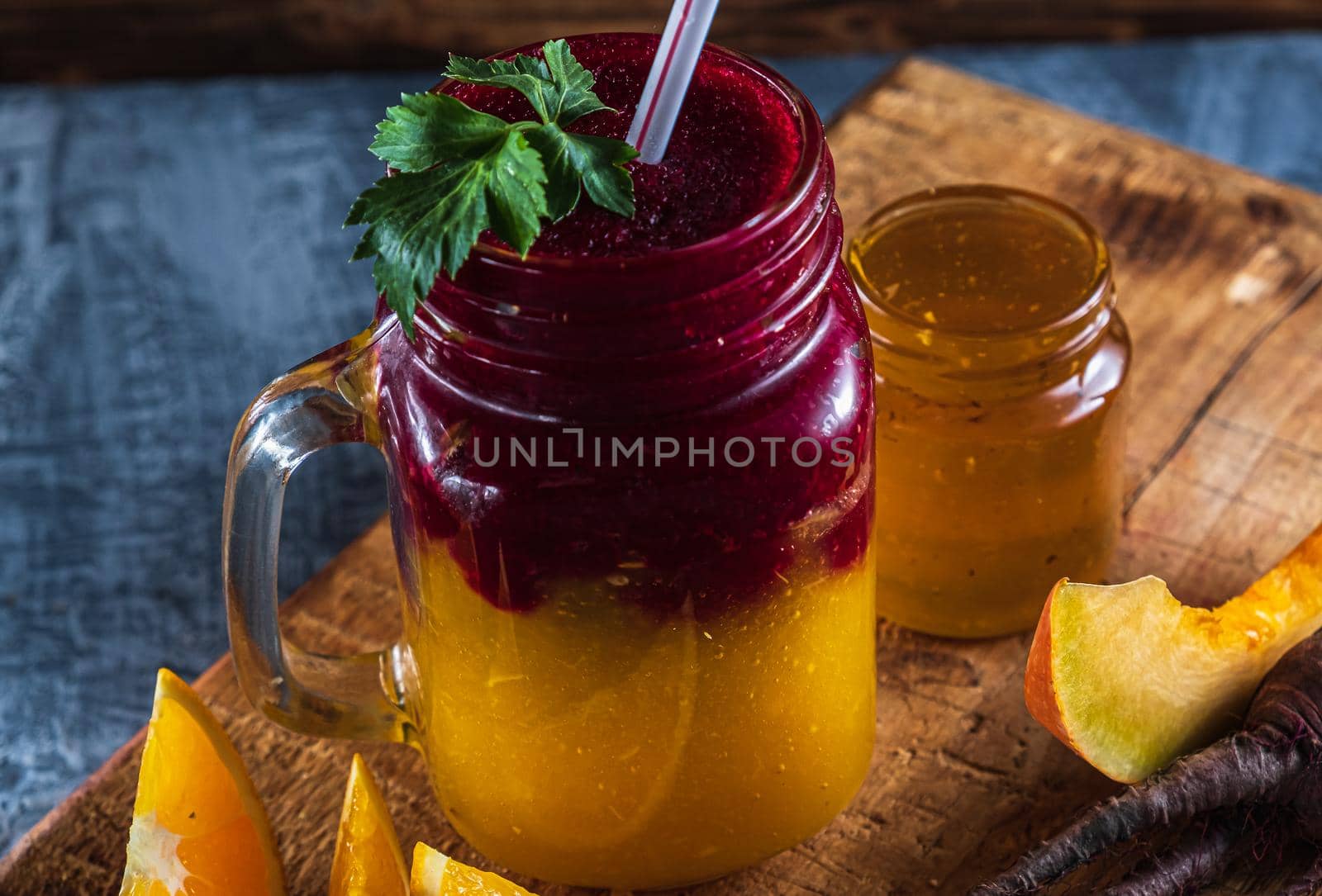 smoothie consists of beetroot pumpkin, orange, celery in mason jar. smoothies are poured in layers. next to it is a jar of honey, beet root, a piece of pumpkin and slices of orange. on a thick wooden board. horizontal orientation.