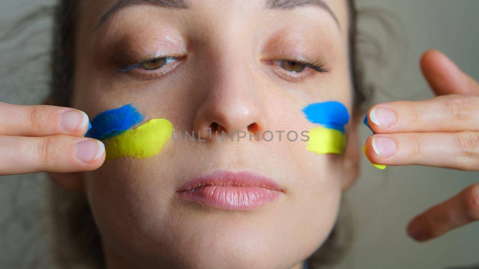 Indoor portrait of young girl with blue and yellow ukrainian flag on her cheek wearing military uniform, mandatory conscription in Ukraine, equality concepts.