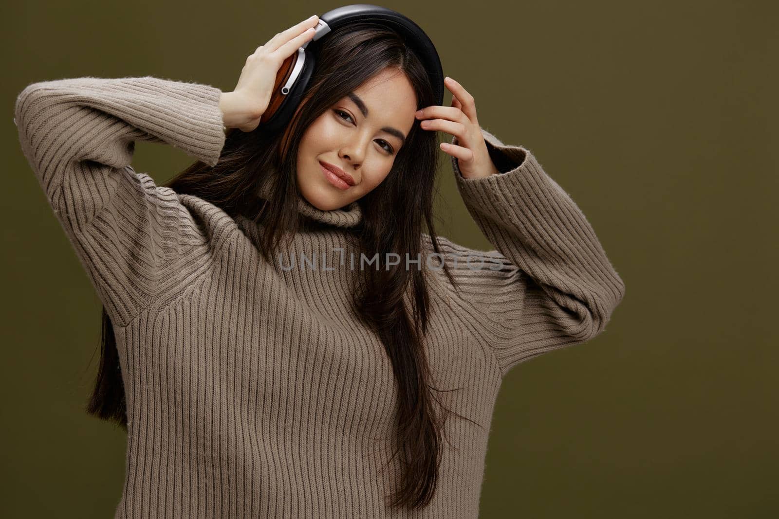 young woman in a sweater listening to music with headphones fun Green background by SHOTPRIME