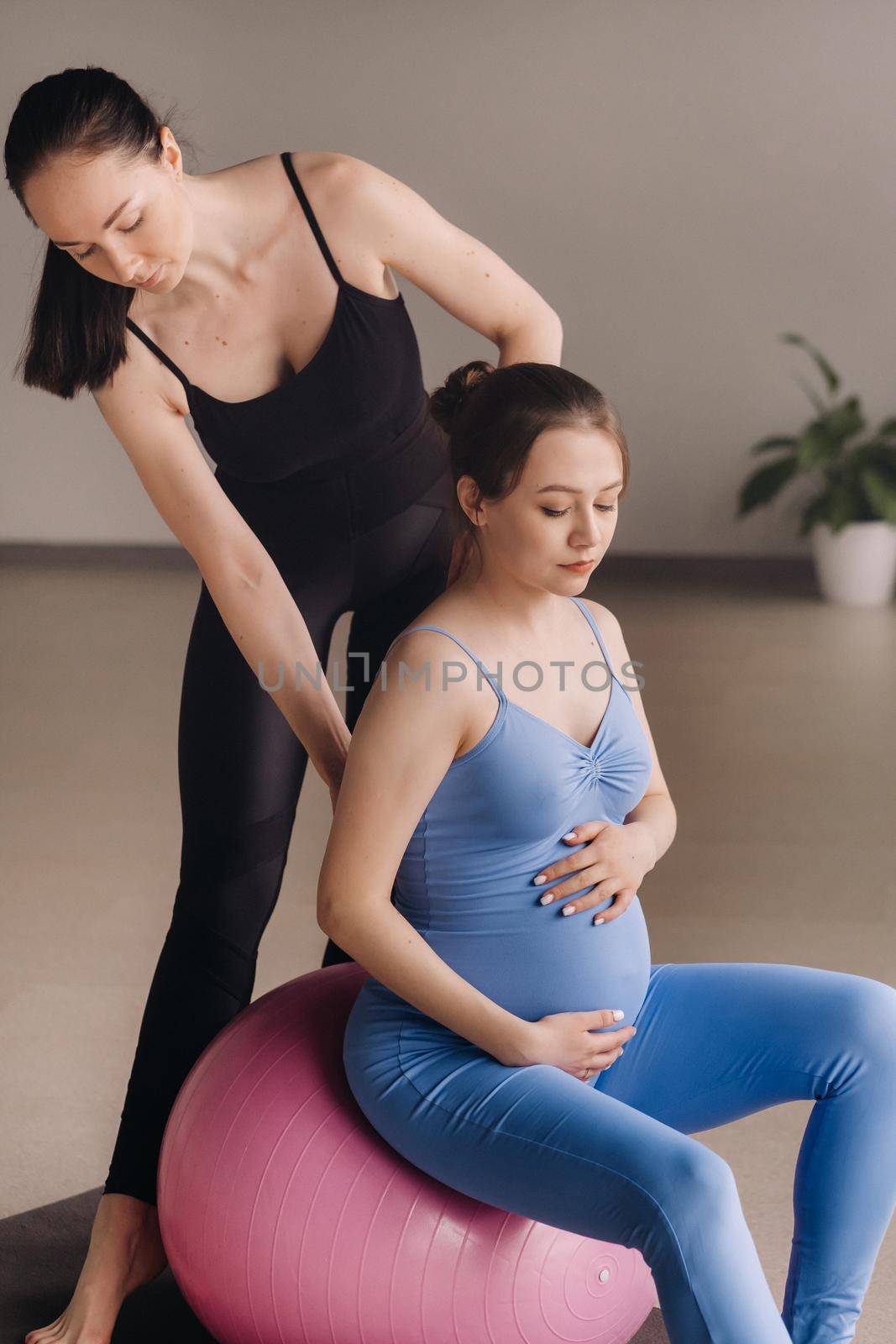 Pregnant woman with a trainer during fitness classes with a ball by Lobachad