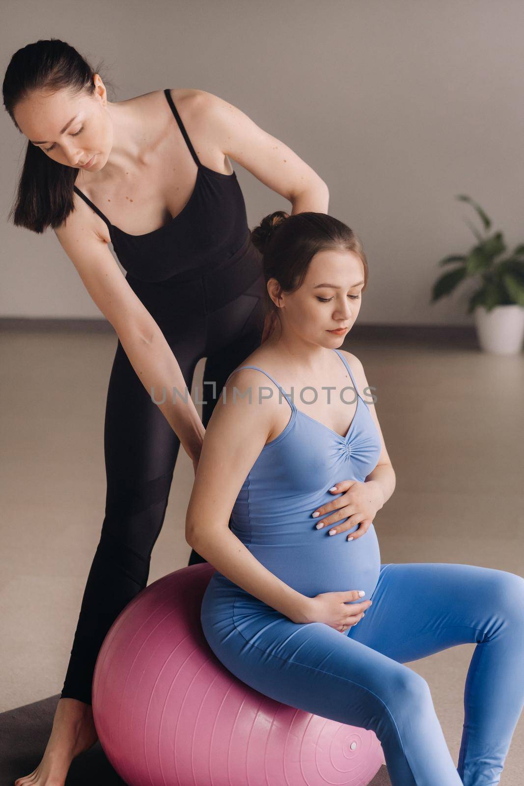 Pregnant woman with a trainer during fitness classes with a ball.