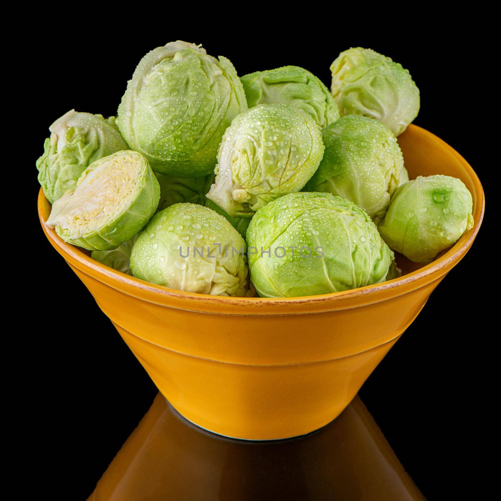 Fresh brussels sprouts on green ceramic bowl isolated on white background.