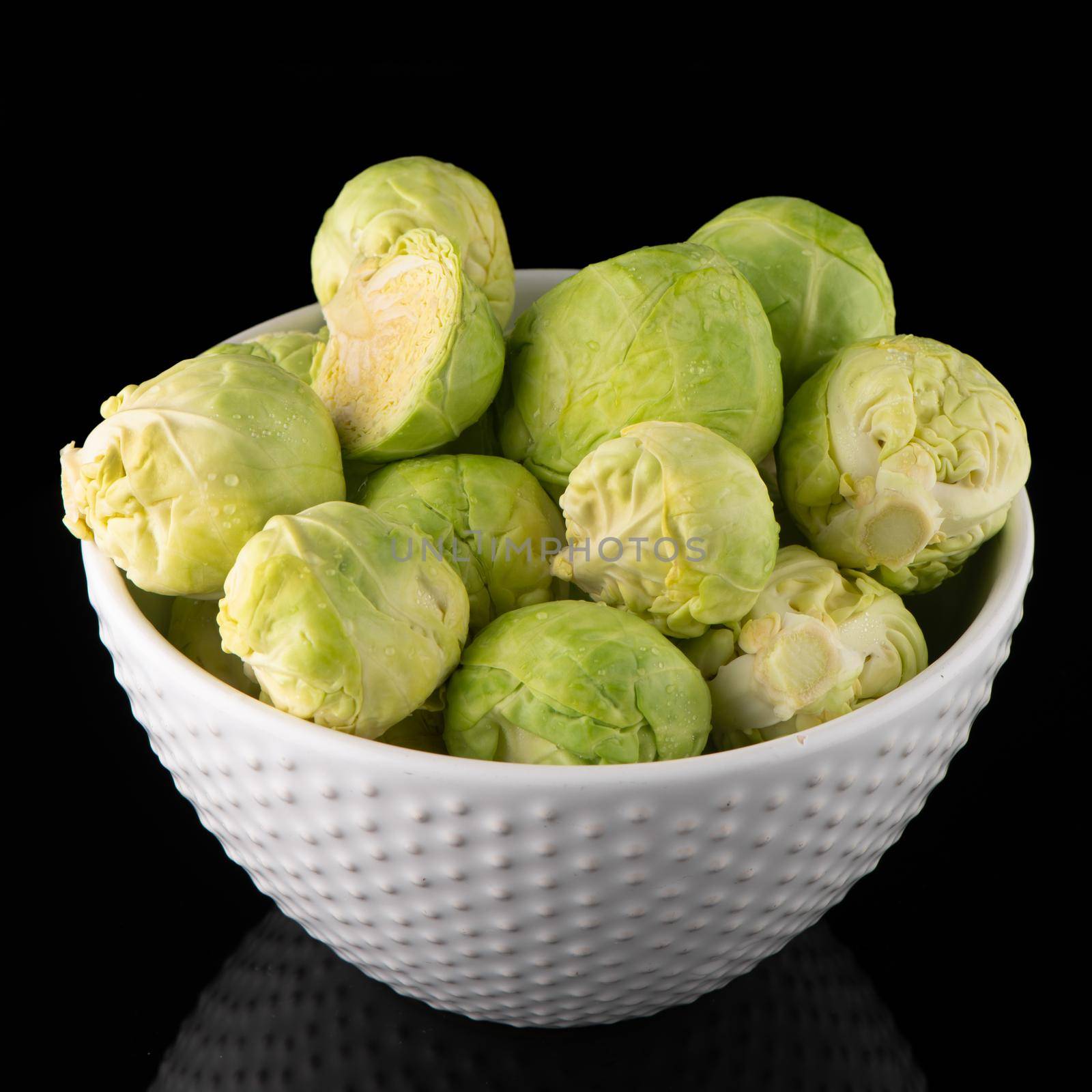 Fresh brussels sprouts on white ceramic bowl isolated on black background.