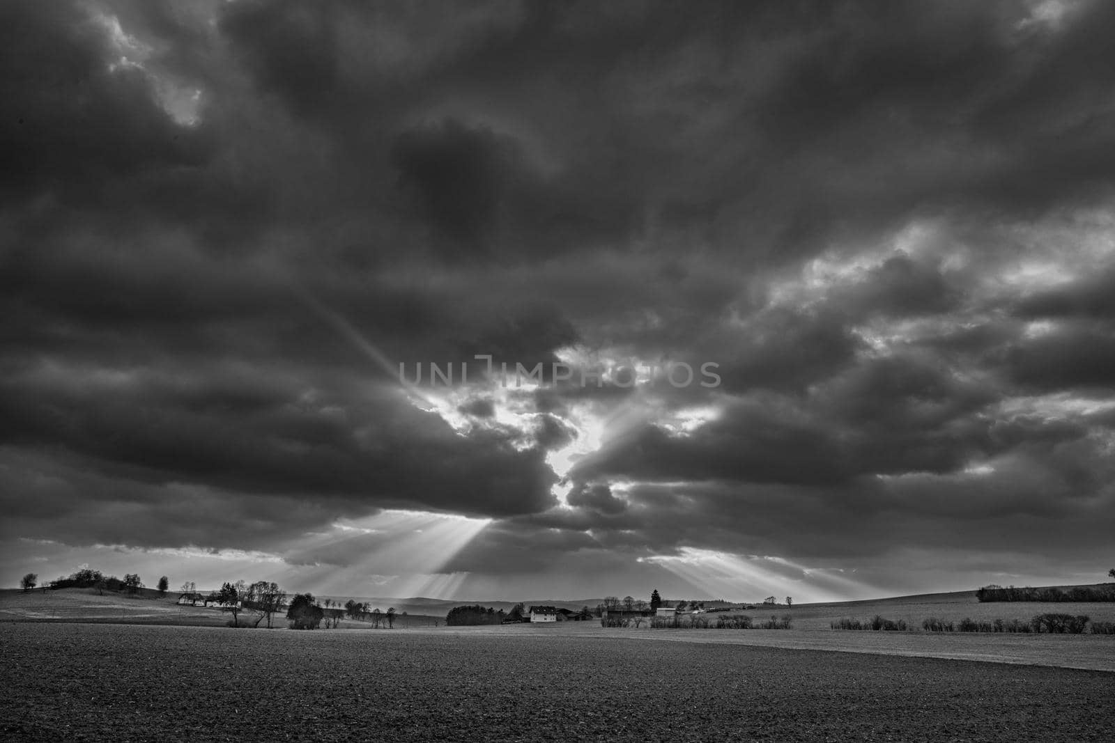 the sun's rays pierce the clouds over the agricultural field by Costin