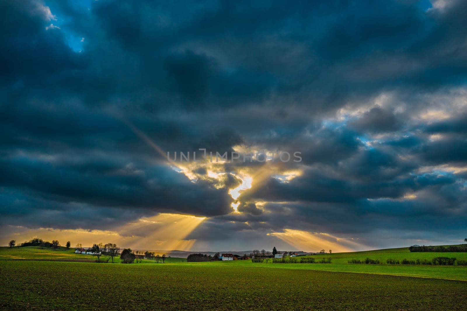 the sun's rays pierce the clouds over the agricultural field by Costin